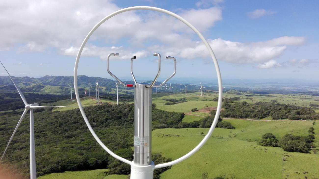 Anemómetro sobre la góndola de un aerogenerador, con el parque eólico Altamira (Costa Rica) al fondo