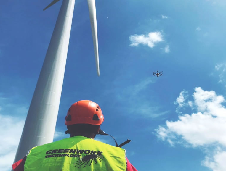 Técnico de Greenwork con casco pilotando un dron junto a un aerogenerador